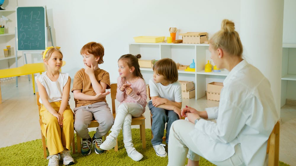 Multi aged montessori children chat with teacher in preschool